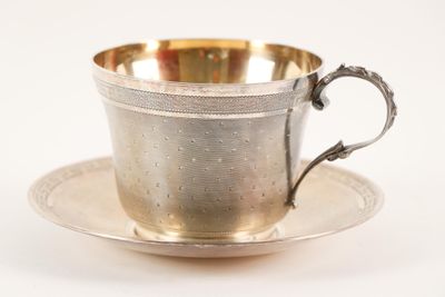 une tasse et une soucoupe anciennes en argent, posées sur une soucoupe, sur fond blanc