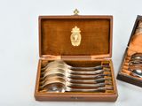 four spoons in a wooden box with a gold emblem on it