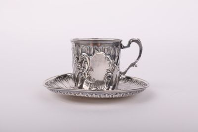 une tasse et une soucoupe argentées posées sur une soucoupe, sur fond blanc