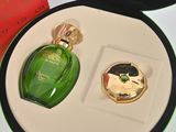 a green bottle of perfume and a gold ring in a box