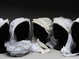 trois mannequins noirs coiffés de bonnets blancs et vêtus de tissu blanc