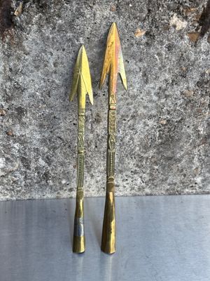 une paire de flèches en laiton posées sur une surface métallique, à côté d'un rocher