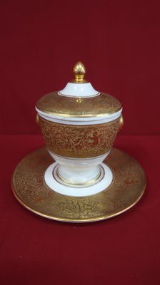 an image of a gold and white bowl and saucer on a red background