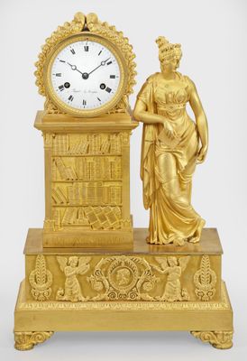 a gold clock with a woman standing next to it