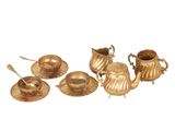 brass tea set with cups, saucers and spoons on a white background