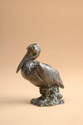 statue of a pelican sitting on a tree stump on a beige background