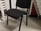 a black chair sitting next to a stack of white chairs