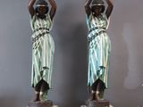 two statues of women holding pots on their heads in front of a gray wall