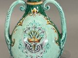 un vase vert orné d'un oiseau, posé sur un fond gris