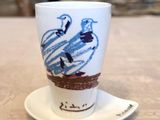 une tasse blanche ornée d'un oiseau bleu, posée sur une soucoupe