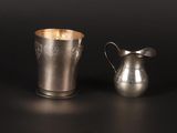 two silver cups and a silver pitcher on a black surface
