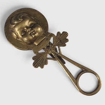 cuillère plaquée or sur laquelle est représentée une tête de poupée, avec une paire de ciseaux devant