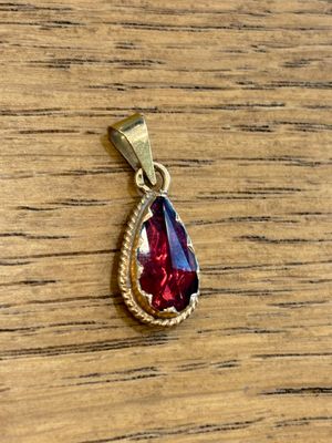 a red and gold tear shaped pendant on a wooden table