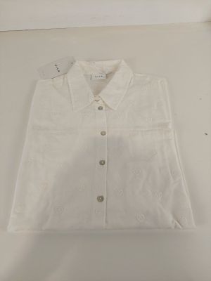 La chemise est blanche et possède un col boutonné.