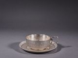 une tasse et une soucoupe en argent posées sur une soucoupe, le tout sur une surface grise