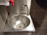 a stainless steel sink in a public restroom with a green trash can