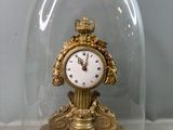une horloge en or sous une cloche en verre, posée sur une table