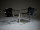 une paire de fauteuils en cuir noir dans une pièce sombre, avec une lampe posée au sol