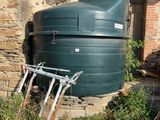 un réservoir d'eau vert posé à même le sol, à côté d'un bâtiment en briques