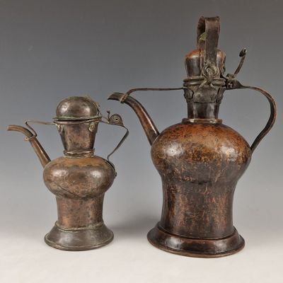 pair of antique metal teapots with handles on a white surface