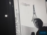 black and white photograph of a woman standing in front of a picture of the eiffel tower
