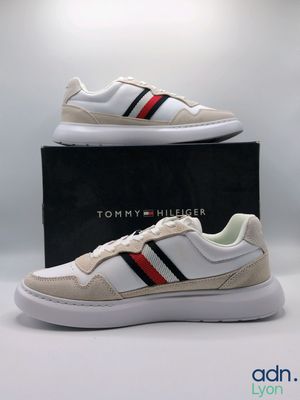 une paire de baskets blanches avec une bande rouge, noire et bleue sur le côté