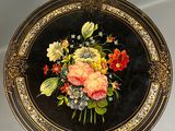 une assiette noire et dorée sur laquelle est représenté un bouquet de fleurs