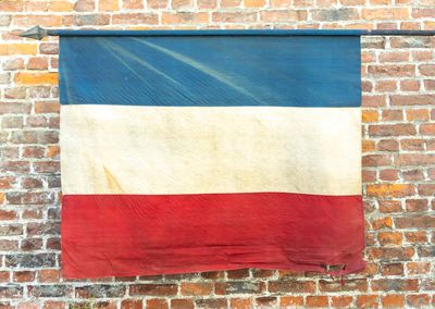 un drapeau rouge, blanc et bleu accroché à un mur de briques