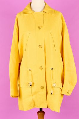 un manteau jaune posé sur un mannequin, devant un fond rose
