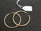 two pairs of gold hoop earrings on a black surface with a price tag