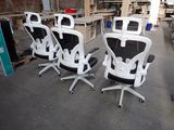 four white office chairs are lined up in a row in a warehouse