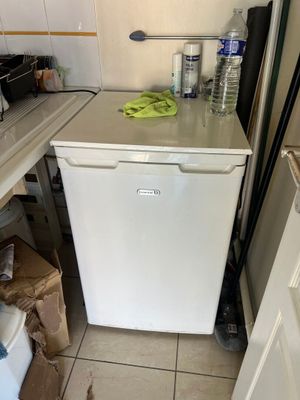 a small white refrigerator in a kitchen with a lot of clutter on the counter