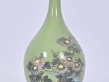 un vase vert orné de fleurs, posé sur un socle en bois