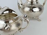 two silver teapots and a sugar bowl on a white surface