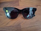 des lunettes de soleil noires de style « œil de chat » posées sur une table en bois, avec un point vert
