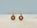 une paire de boucles d'oreilles en or serties de diamants, posées sur une surface en marbre