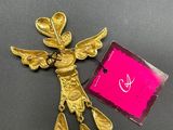 a close up of a gold angel brooch with a pink tag