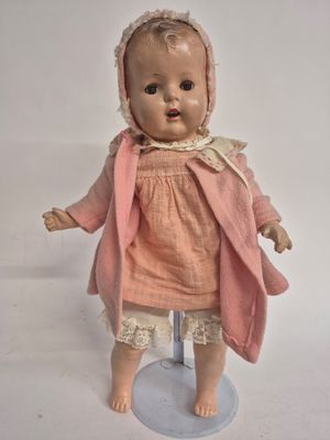 a small doll with a pink dress and bonnet on a stand