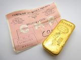 un vieux lingot d'or posé à côté d'un bout de papier sur une surface blanche