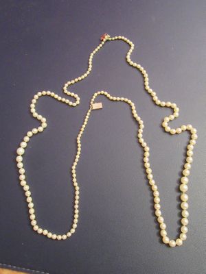 a white pearl necklace with a gold clasp on a black surface