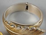 a gold ring with a feather on it next to a gold watch
