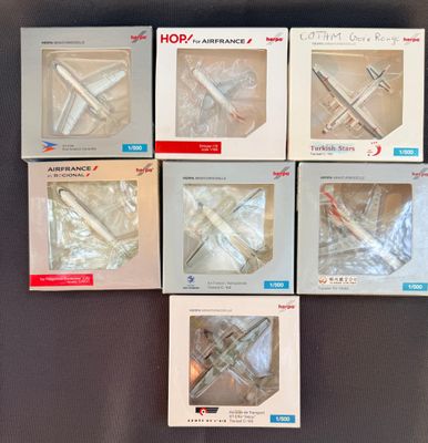 Six boîtes contenant divers modèles réduits d'avions sont posées sur une table.