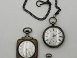 trois montres de poche anciennes et une chaîne posées sur une surface blanche