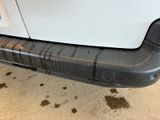 the rear bumper of a white van with dirty paint on it