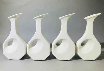 quatre vases blancs sont alignés sur une surface grise