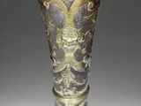 an old silver vase sitting on top of a table next to a gray wall