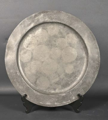 une assiette en argent posée sur un socle noir, sur un fond gris
