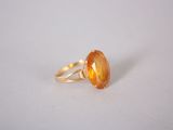 a close up of a ring with an orange stone on a white surface