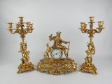three gold colored candlesticks and a clock on a table
