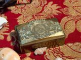une boîte dorée posée sur un tapis rouge, entourée de coquillages